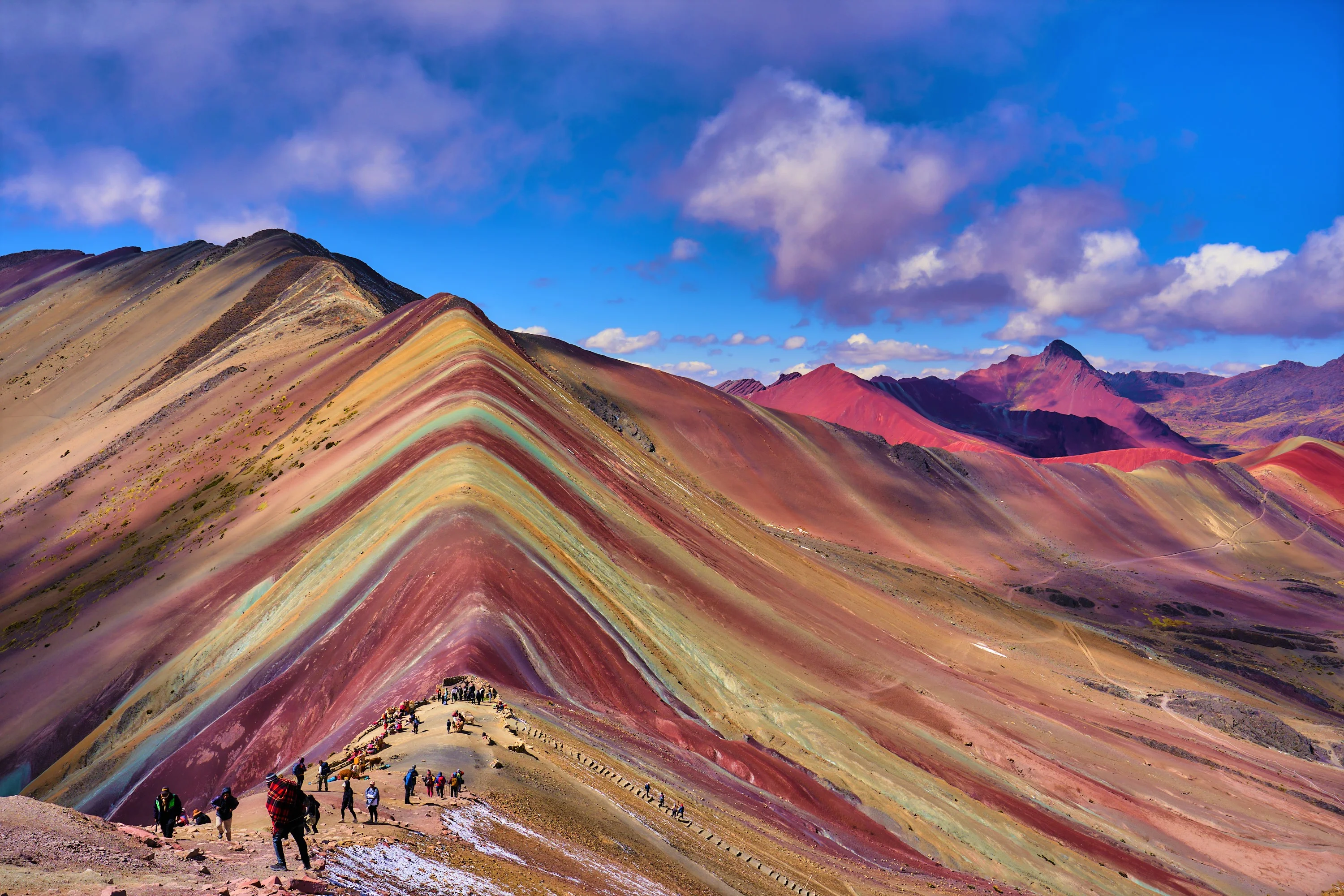 Panoramic view of Rainbow Mountain in Cusco, Peru, with visitors walking along the colorful ridge