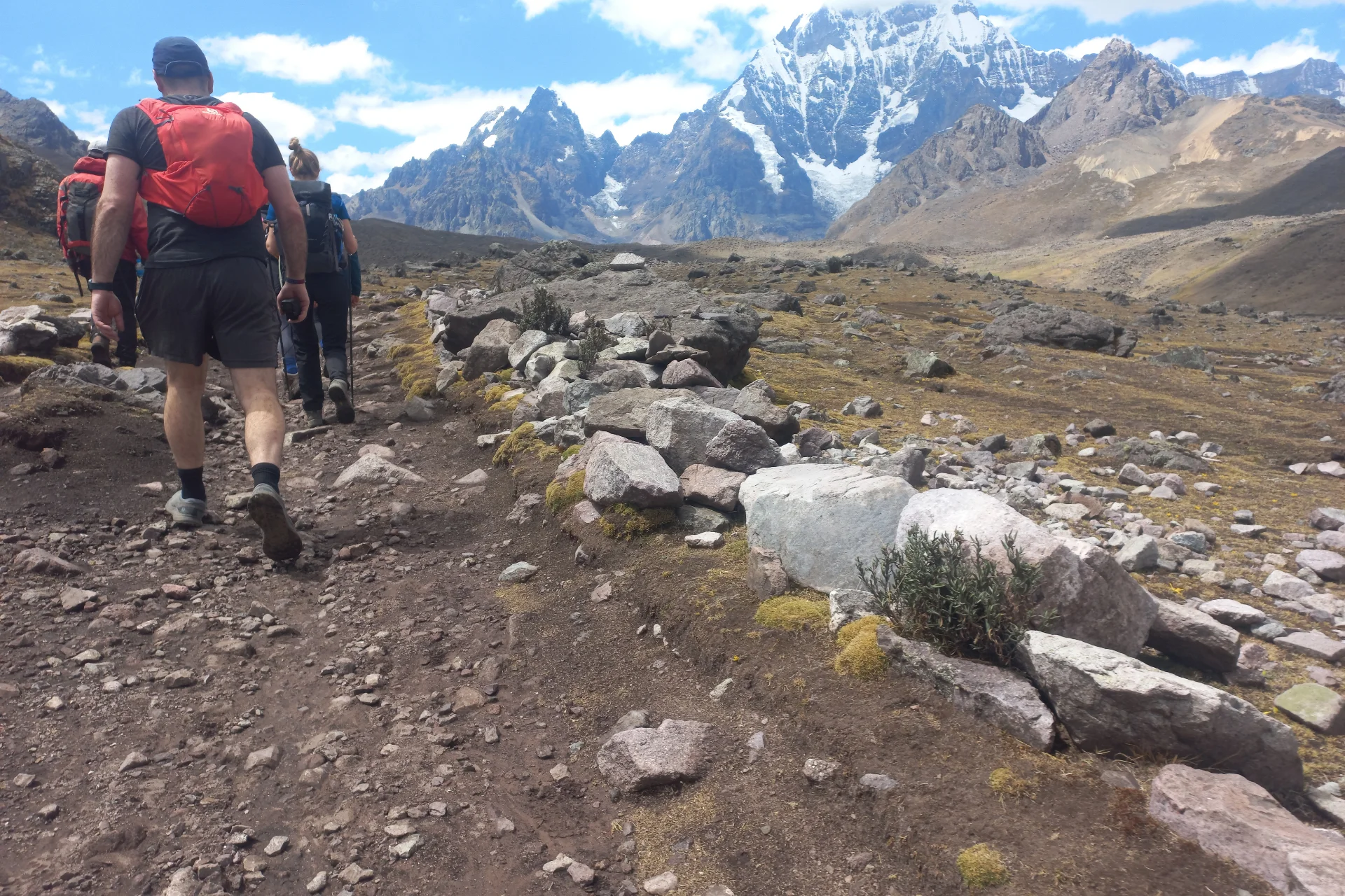 Hikers following a rocky trail beneath snow-covered peaks during the Ausangate 7 Lakes Tour from Cusco.