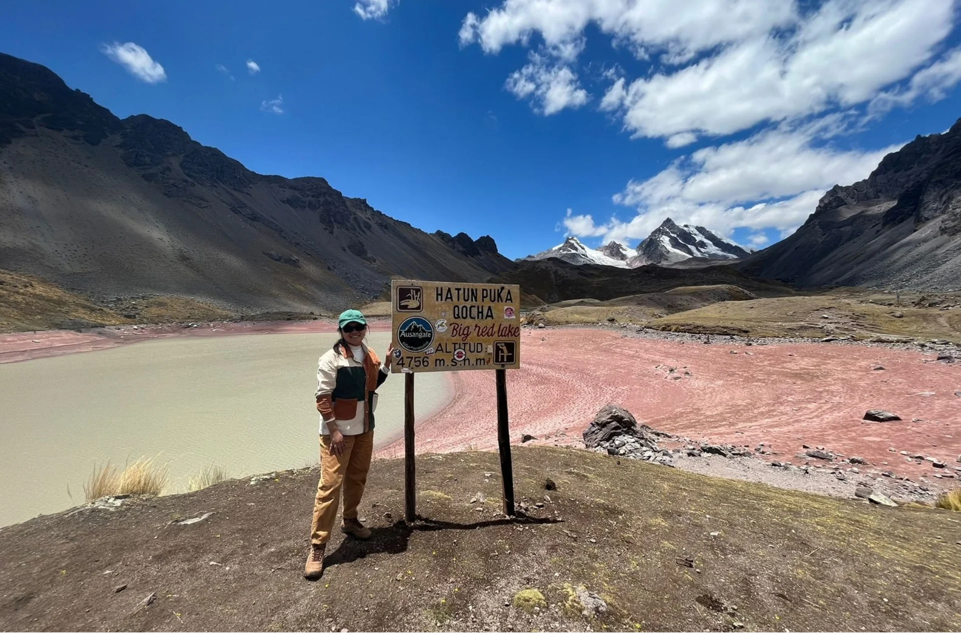 Traveler beside the Hatun Puka Qocha sign, known as Big Red Lake, during the Ausangate 7 Lakes Tour in Cusco.
