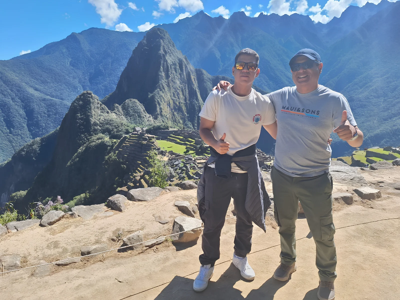 Two travelers posing at Machu Picchu with the citadel and Andean mountains in the background