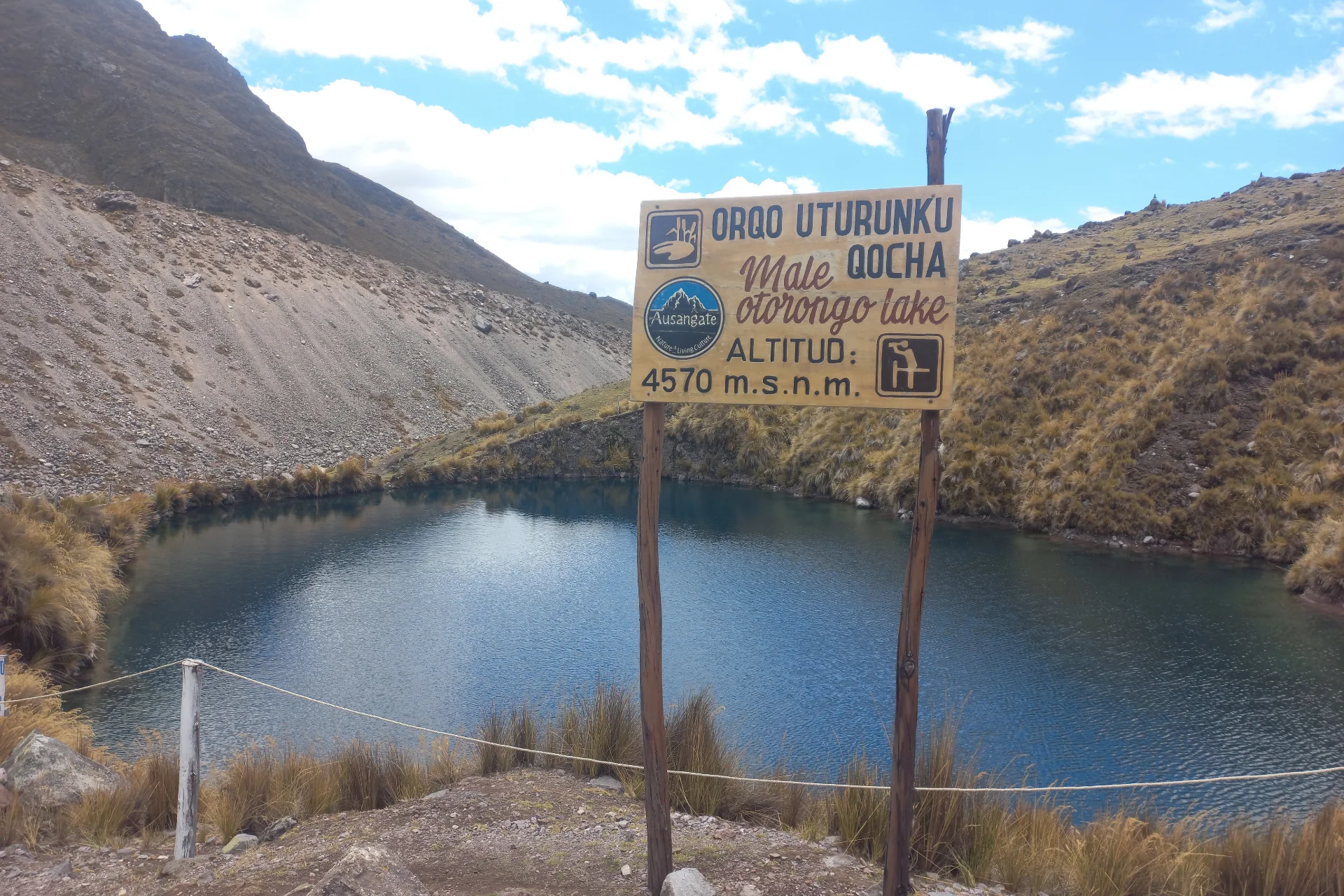 View of Orqo Uturunku Qocha lake and its trail sign along the Ausangate 7 Lakes route near Cusco.