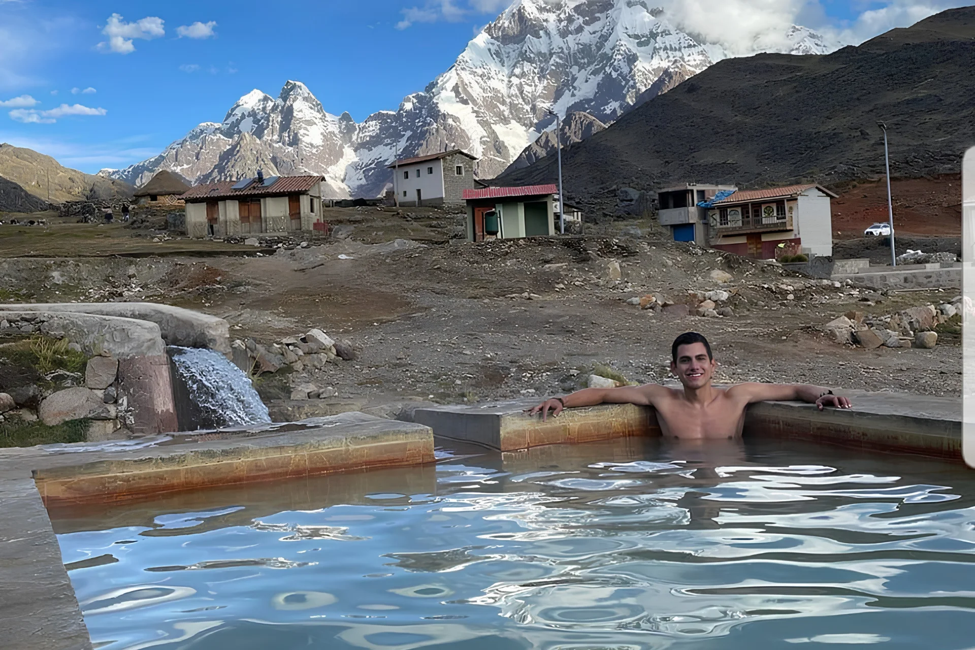 Traveler relaxing in the Pacchanta hot springs with snow-covered Ausangate mountains in the background.