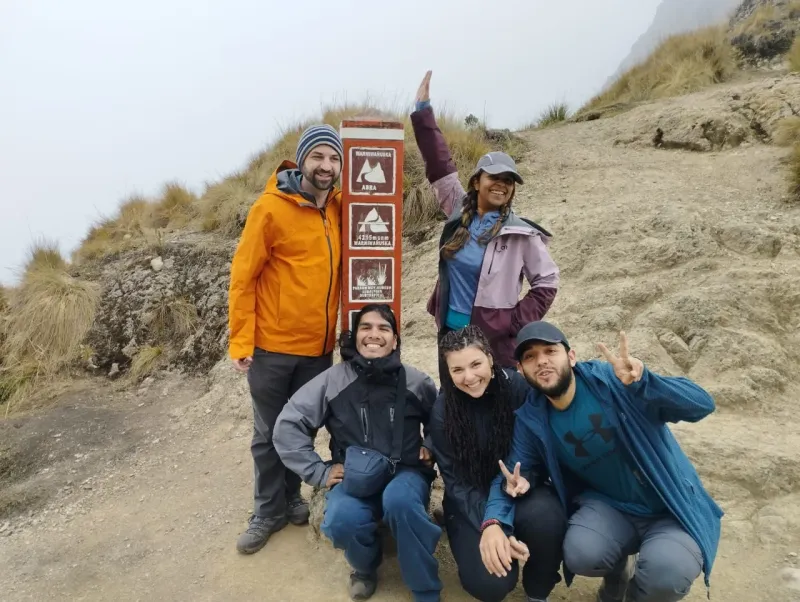 Viajeros en el Camino Inca a Machu Picchu junto a una señal del sendero, rodeados de montañas y neblina andina | Inca Culture Travel