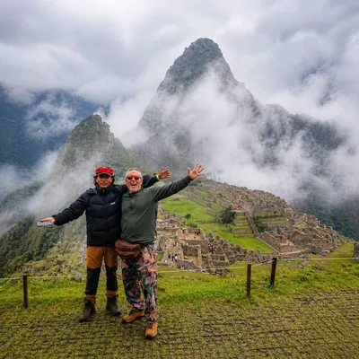 Dos viajeros posando con Machu Picchu y las montañas andinas cubiertas de neblina al fondo | Inca Culture Travel