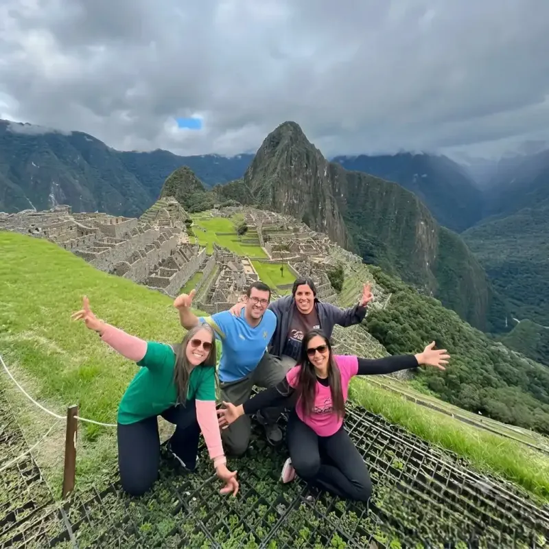 Grupo de amigos posando con los brazos abiertos en el clásico mirador de la ciudadela de Machu Picchu, Perú | Inca Culture Travel