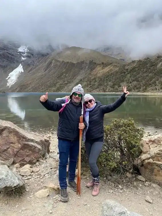 Grupo de viajeros posando frente a la Laguna Humantay con montañas y cielo nublado | Inca Culture Travel
