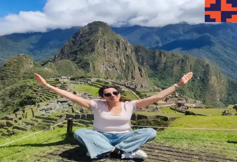 Mujer sentada sobre el césped contemplando la montaña Huayna Picchu y las antiguas ruinas de Machu Picchu | Inca Culture Travel