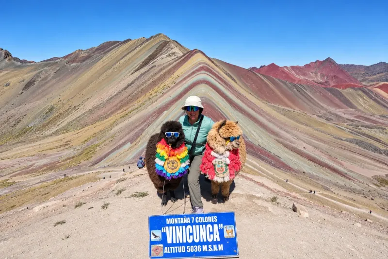 Travelers posing next to the Rainbow Mountain Vinicunca sign in Peru